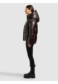 Glansig, mörkbrun vadderad jacka med luva, med dragkedja framtill och elastiska ärmslut, kombinerad med tåliga svarta leggings och knähöga svarta stövlar.