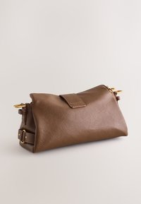 Bruine leren clutch tas met gouden hardware, vouwklep en afneembare band op een effen lichte achtergrond.