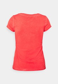 T-shirt z krótkim rękawem w koralowym kolorze, wykonany z bawełny, z okrągłym dekoltem i subtelnie postarzanym teksturem. Widok z tyłu ukazuje gładką tkaninę i szwy.