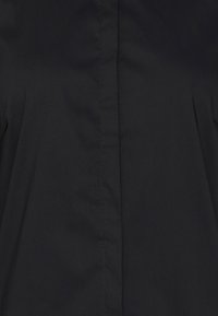 Chaqueta negra con una textura suave, corte recto y detalles de costura sutiles en el frente. Sin hardware ni patrones visibles.