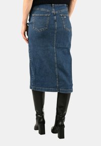 Gonna di jeans con silhouette dritta, lunghezza fino al polpaccio e tasche posteriori, abbinata a stivali neri in pelle al ginocchio.