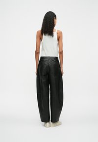Zwarte leren wijde broek met een hoge taille, gedetailleerde stiksels en twee achterzakken, gecombineerd met een witte mouwloze top.