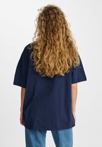 Mörkblå oversized t-shirt i mjuk bomullsmaterial, med korta ärmar och avslappnad passform. Bakifrån visas minimal detaljering och en slät textur.