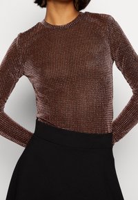 Långärmad topp i ett glansigt brunt ribbat material, med rund halsringning och figurnära siluett, kombinerad med en svart högmidjad kjol.