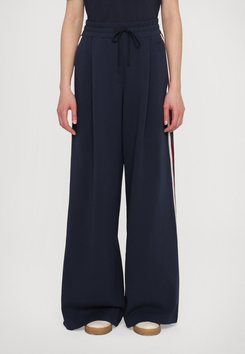 Navy wide-leg pants with a drawstring waistband, featuring side stripes in red and white, made from a soft, textured material.