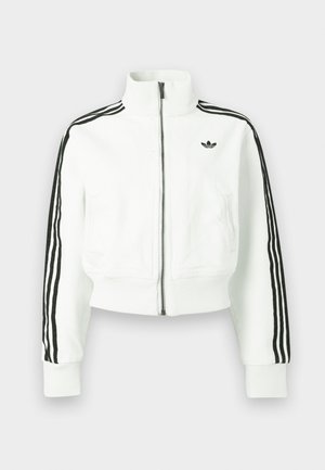 Kort vit jacka med hög krage, dragkedja framtill och svarta tre-randiga detaljer på ärmarna. Har en liten svart logga på bröstet.