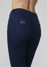 Tmavomodré džíny z denimu so stredne vysokým pásom. Medzi funkcie patrí textúrovaný pás, dve zadné vrecká a čierny štítok ako akcent.