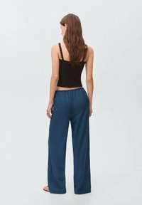 Svart crop top med vågiga kanter och löst sittande marinblå byxor med elastiskt midjeband, sett bakifrån.