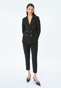 Blazer de dos botones con rayas negras y plateadas, de corte ajustado, combinado con pantalones slim fit a juego y tacones negros de punta.