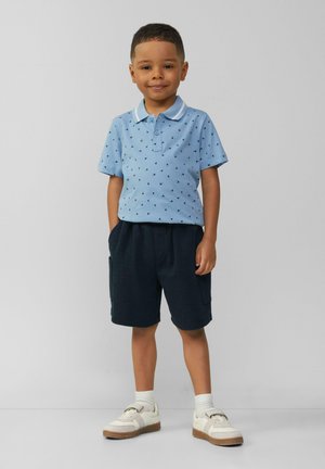 Blauwe poloshirt met een kraag en kleine patronen, gecombineerd met donkere shorts en witte sneakers met een gestructureerde zool.