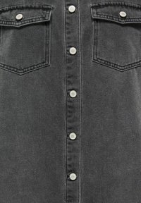 Zwarte denim blouse met een knoopsluiting aan de voorkant, twee borstzakken en zilveren drukknopen. De stof heeft een zachte textuur en minimale vervaging.