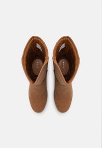 Bottes chelsea en cuir marron avec une doublure en fourrure marron douce. Bout arrondi et tige de hauteur moyenne. Extérieur lisse sans quincaillerie visible.