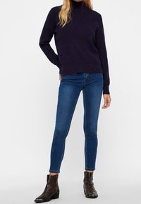 Laivastonsininen pooloneule, teksturoitu neulos, yhdistetty istuviin sinisiin farkkuihin ja tummiin nilkkureihin, joissa on matelijatäyteinen kuviointi. Yksinkertainen ja moderni asukokonaisuus.