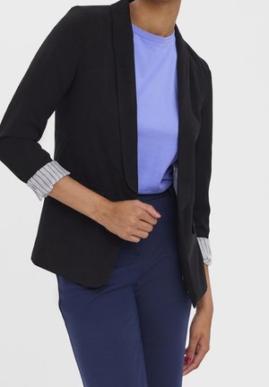 Black blazer with a fitted design, featuring striped cuffs under rolled sleeves. Paired with a light blue t-shirt and navy pants.
