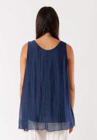 Top senza maniche blu navy in un tessuto leggero e testurizzato con scollatura sul retro, caratterizzato da un orlo trasparente leggermente più lungo.