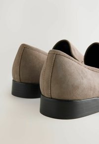 Une paire de chaussures de ville à talons bas en daim taupe avec des semelles noires, vue de l'arrière sur un fond blanc.