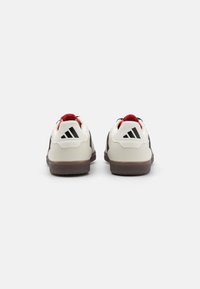 Niskie sneakersy z białą cholewką, czarnymi akcentami, czerwonymi detalami i czarnym logo z trzema paskami. Teksturowana podeszwa z gumy.