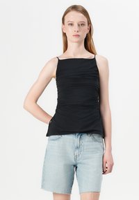 Zwarte mouwloze top met geplooide structuur, vierkante halslijn en dunne bandjes, gecombineerd met lichtblauwe denim shorts.