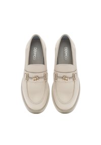 Mocasines de cuero beige con herrajes plateados, que cuentan con una correa decorativa y punta redondeada, situados sobre una suela de color claro.