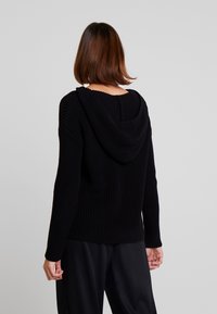Felpa nera a maglia con finitura testurizzata, caratterizzata da una cucitura sul retro, maniche lunghe e una vestibilità comoda. Nessuna decorazione aggiuntiva presente.
