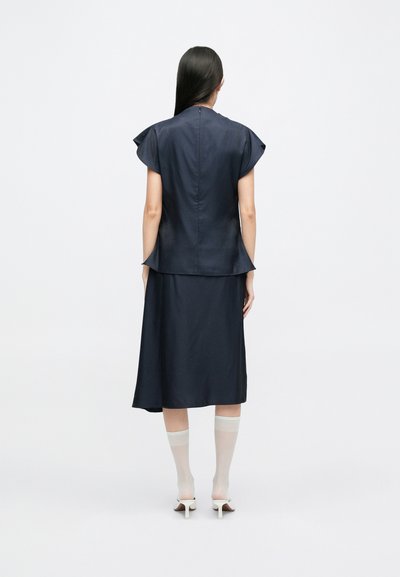 Mørkeblå todelt kjole med korte flæseærmer; glat tekstur; A-linje silhuet; parret med gennemsigtige hvide knæhøje sokker og hæle.