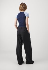 Haut court bleu marine et clair, ajusté au corps. Pantalons larges noirs avec poches arrière et accents de boutons. Coupe décontractée.