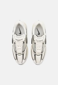 Bāli sporta apavi baltā krāsā ar melniem akcentiem, kas izgatavoti no sieta un sintētiskiem materiāliem, ar teksturētu zoli un izteiktu Nike logotipu uz mēles.