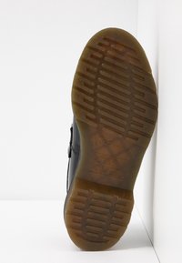 Semelle d'une botte noire avec caoutchouc brun translucide, motif de bande de roulement rainuré, et marquages en relief de la marque et de la taille.