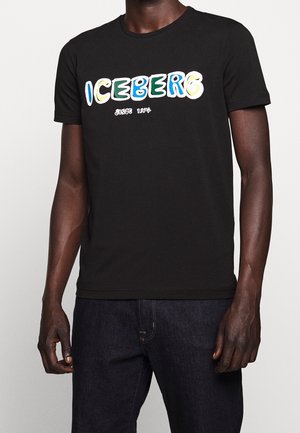 T-shirt noir à manches courtes porté par une personne, avec l'inscription « ICEBERG depuis 1974 » en grandes lettres colorées et ludiques sur la poitrine.