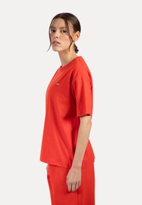 T-shirt rossa in cotone con collo a giro, maniche corte e un logo discreto sul petto. Vestibilità leggermente rilassata con una texture morbida.