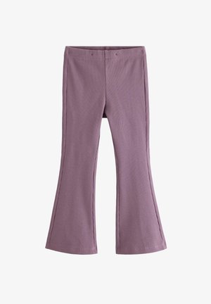 Ung pige står med en lyserødt mønstret fluffy rygsæk, iført lilla blomstret top og bukser, smilende og holder en rem.