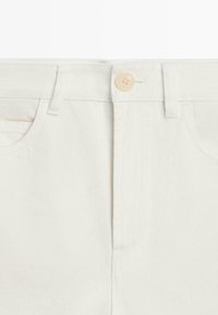 Jean en denim blanc taille haute avec fermeture à boutons, passants pour ceinture et poches avant.