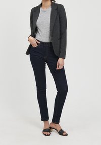 Šedé tričko, tmavý blejzr, tmavé skinny džíny a černé sklápěcí sandály. Hladká tkanina, dobře padnoucí střih, minimální detaily a neutrální barvy.