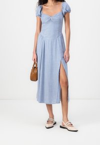 Blå rutigt midiklänning med puffärmar, figurnära bodice och slits på sidan. Kombinerad med beige slip-on skor och en liten brun handväska.