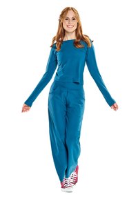 Türkiz színű, hosszú ujjú felső és azonos színű, bő szárú nadrág sima anyagból, piros tornacipővel párosítva. Az outfit laza szabású.