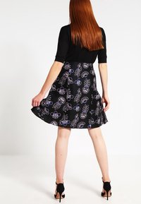 Sort nederdel med blomsterprint i lilla og blå. Har et udskudt design, blødt stof og er parret med en tætsiddende sort top.
