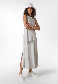 Robe sans manches gris clair avec un ourlet asymétrique et des fentes latérales, associée à des baskets à plateforme blanches et une casquette blanche.