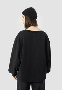 Black oversized sweatshirt with a wide neckline and dropped shoulders. The fabric appears soft, featuring a subtle seam detail on the back.