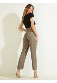 Pantalones gris claro de cintura alta, de pierna recta, con un parche de cuero en la parte posterior. También se observa una blusa negra texturizada y unos tacones de aguja estampados.