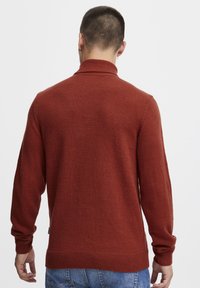Pulover tricotat de culoare ruginită, cu guler înalt, mansete și tiv cu un model striat. Prezintă o textură netedă și o croială lejeră. Vedere din spate.