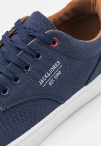 Navy canvas sneaker with brown interior lining, featuring blue and burgundy eyelets, white sole, and "JACK&JONES EST.1990" logo detail.
