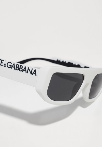 Valged prillid nurgeliste raamidega, tumedate läätsedega ja rihmaga. Küljel on mustalt trükitud kaubamärk "DOLCE & GABBANA".