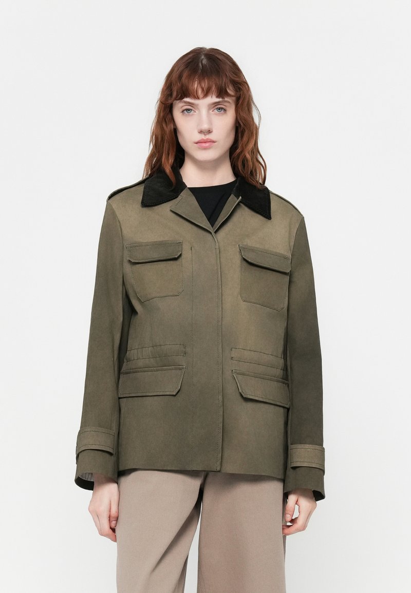 Casaco verde-azeitona com um colarinho de veludo preto, bolsos frontais e mangas longas. Textura suave com um design estruturado.
