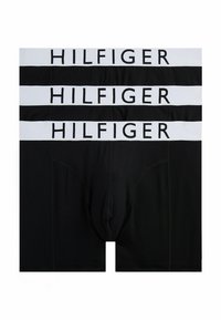Boxer ajustados negros con cinturilla elástica blanca. Varios pares apilados, con el logo "HILFIGER" en texto negro en la cinturilla. Tejido suave.