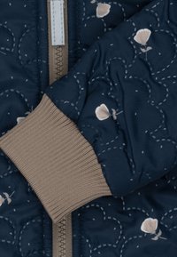 Marineblauer, gesteppter Mantel mit Blumenmustern, beige gerippte Bündchen und einem zentralen Reißverschluss. Glatte Textur mit gesteppten Akzenten und einem gemütlichen Design.