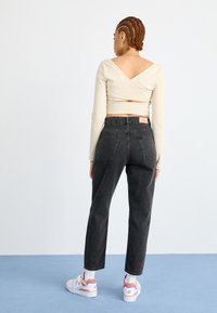 Jeans neri a vita alta con una vestibilità rilassata, dotati di tasche posteriori e un'etichetta in pelle. Abbinati a un top avvolgente beige chiaro e sneakers bianche.