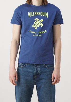 T-shirt en coton bleu marine avec un graphisme néon de tortue et le texte "VILEBREQUIN À SAINT-TROPEZ DEPUIS 1971." Style classique à col rond.