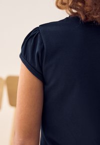 Dunkelblaues T-Shirt mit kurzen, puffigen Ärmeln, aus weichem Material gefertigt. Der Rücken zeichnet sich durch ein klares Design mit subtilen Nähdetails aus.