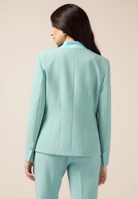 Mintgrüner Blazer mit tailliertem Design, scharfen Revers und Nahtdetails, mit kontrastierenden Knöpfen an den Ärmeln.