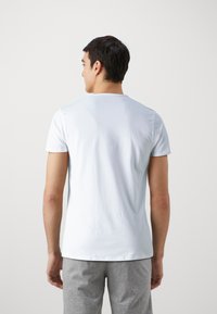 T-shirt bleu clair à manches courtes en coton doux, avec un col rond et une coupe décontractée. Associé à un pantalon gris, vu de l'arrière.